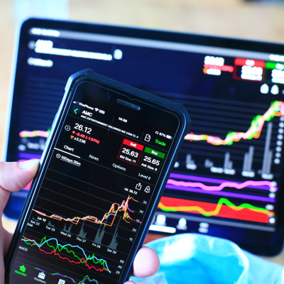 The image depicts a person holding a smartphone, intently focused on the screen. Their fingers are hovering over the device, likely navigating through a stock market trading app or website. The individual's focused expression suggests their active engagement in the trading process. This image effectively conveys the convenience and accessibility of modern stock market trading, allowing individuals to monitor and manage their investments from the comfort of their mobile devices. stock market blogs